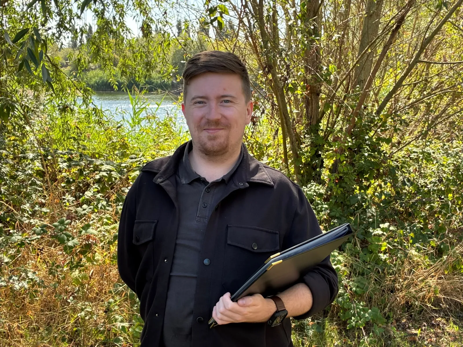 Luke Webb outdoors holding his ceremony folder